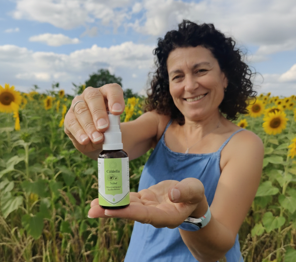 Glueckliche Frau 50 Jahre zeigt Caldelia Schlaf Mundspray mit Bachbluten im Sonnenblumenfeld
